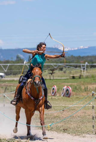 Image of a customer engaging in a unique activity with her horse, incorporating archery, showcasing a skillful and adventurous interaction between the rider and her equine companion.