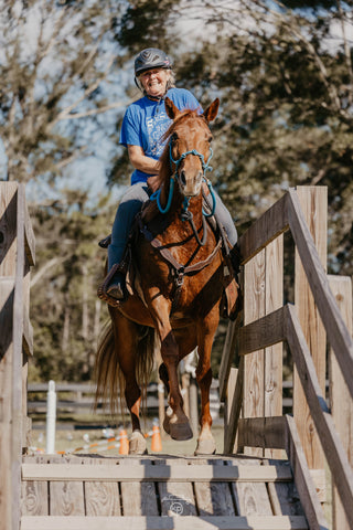 A customer confidently crossing a bridge in the obstacle course during a Horse Help retreat, building trust and overcoming challenges with their horse.