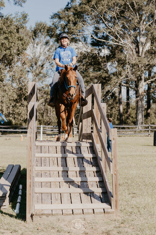 A customer confidently crossing a bridge in the obstacle course during a Horse Help retreat, building trust and overcoming challenges with their horse.