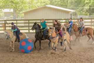 Image of Kelsey Gascon and retreat participants enjoying a game of horse soccer in the arena, fostering camaraderie and equestrian fun during the retreat.