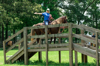 A customer confidently crossing a bridge in the obstacle course during a Horse Help retreat, building trust and overcoming challenges with their horse.