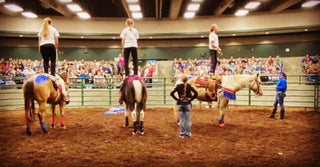 Image of Kelsey Gascon and Trixie Chicks Trick Riders confidently demonstrating tricks during a Trick Riding 101 Clinic, showcasing their expertise and entertaining the audience with skilled equestrian performances.
