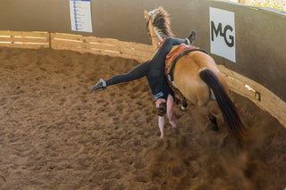 Kelsey Gascon confidently showcasing her impressive Trick Riding skills in a round pen during a mesmerizing performance at Gascon Horsemanship. The dynamic display captures her expert horsemanship and the beauty of the intricate tricks she effortlessly executes.