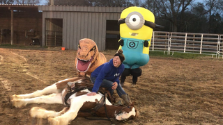Image of Kelsey Gascon posing happily with a horse, accompanied by amusing figures in T-rex and Minion costumes in the background, creating a cheerful and lighthearted equestrian scene.